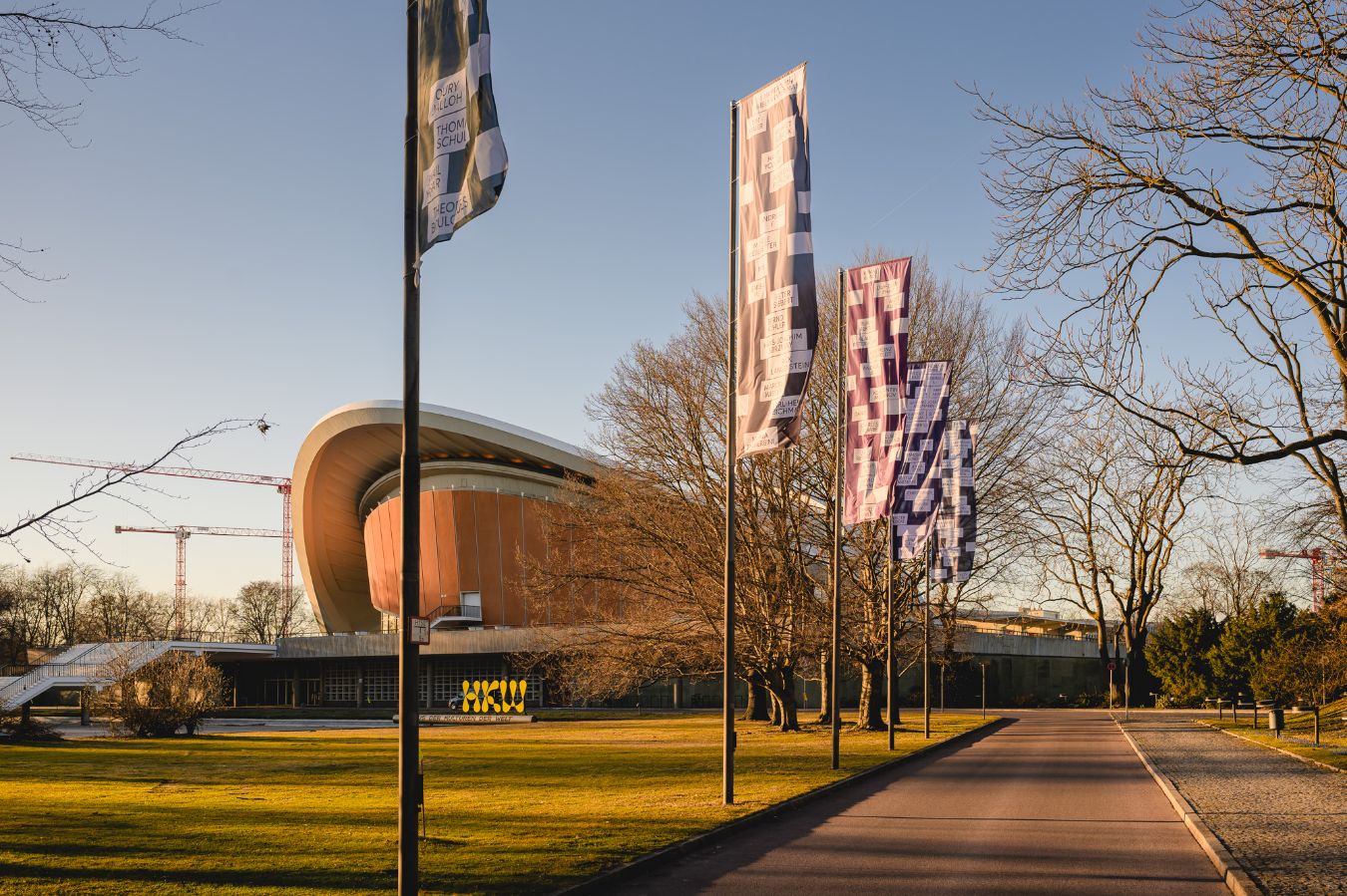 Au&szlig;enansicht Haus der Kulturen der Welt (HKW) mit Flaggenserie von Ulf Aminde:&nbsp;Klage (Gedenken an die Todesopfer rechter Gewalt in Deutschland seit 1990 // 2. Aktivierung) (2024&ndash;), Serie aus 16 Flaggen, Ma&szlig;e variabel
