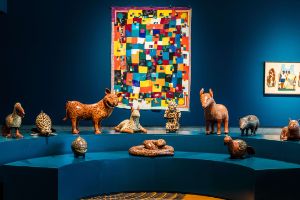 Celia Vasquez Yui with Diana Ruiz Vasquez,&nbsp;The Council of the Mother Spirits of the Animals&nbsp;(2020/23), installation, coil-built pre-fire slip-painted clay, vegetal resins. Courtesy of the artists and Shipibo Conibo Center, New York; Bastin Santan Diggekar, Untitled (2023), textile, hand-stiched siddi kavand with embroidery, 229 x 280 cm. Courtesy of the artist. Installation view of the exhibition, Haus der Kulturen der Welt (HKW), 2023.
