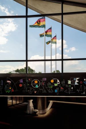 Tanka Fonta, The Cosmogenic Interconnectedness &#39;How Did We Talk Before the Roman Alphabet?&#39; The Picto-Sonic Dialogues I, mural (2023), dimensions vary, comprised of 9 elements. Courtesy of the artist. Olu Oguibe,&nbsp;DDR: Decarbonize, Decolonize, Rehabilitate (2023), textile work, 3 flags, 4.5 x 7 m each. Courtesy of the artist. Installation view of the exhibition, Haus der Kulturen der Welt (HKW), 2023.&nbsp; &nbsp; &nbsp;
